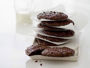 Literally tempting. The cookies are a dark chocolate color while in a completely white and light environment.  The cookies are stacked on the side of the photo and the cup of milk in the background is blurred.
